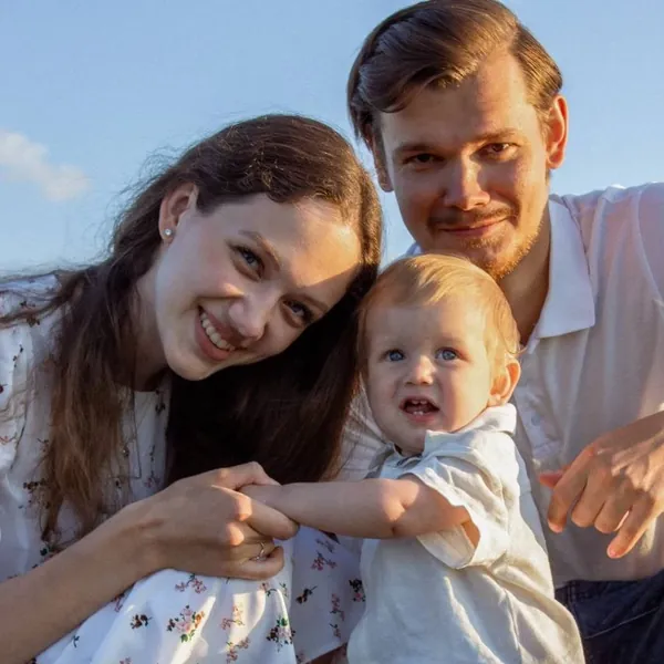 Tim with his wife and their son Timofey, close together outdoors in warm sunshine.